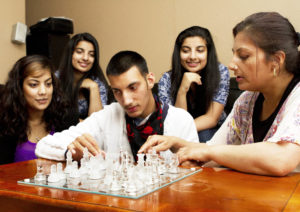 Image of a young person with additional support needs playing chess with friends and family